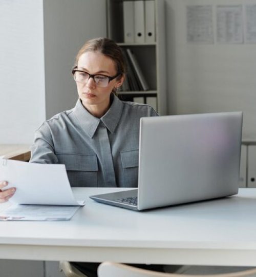 serious-female-visa-service-worker-wearing-eyeglasses-sitting-desk-office-looking-through-appl_249974-12873